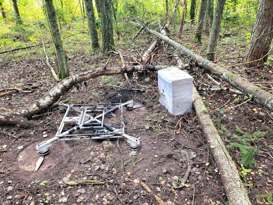 The burned drone frame and a foam-wrapped cigarette bundle in the forest near Antaniškės