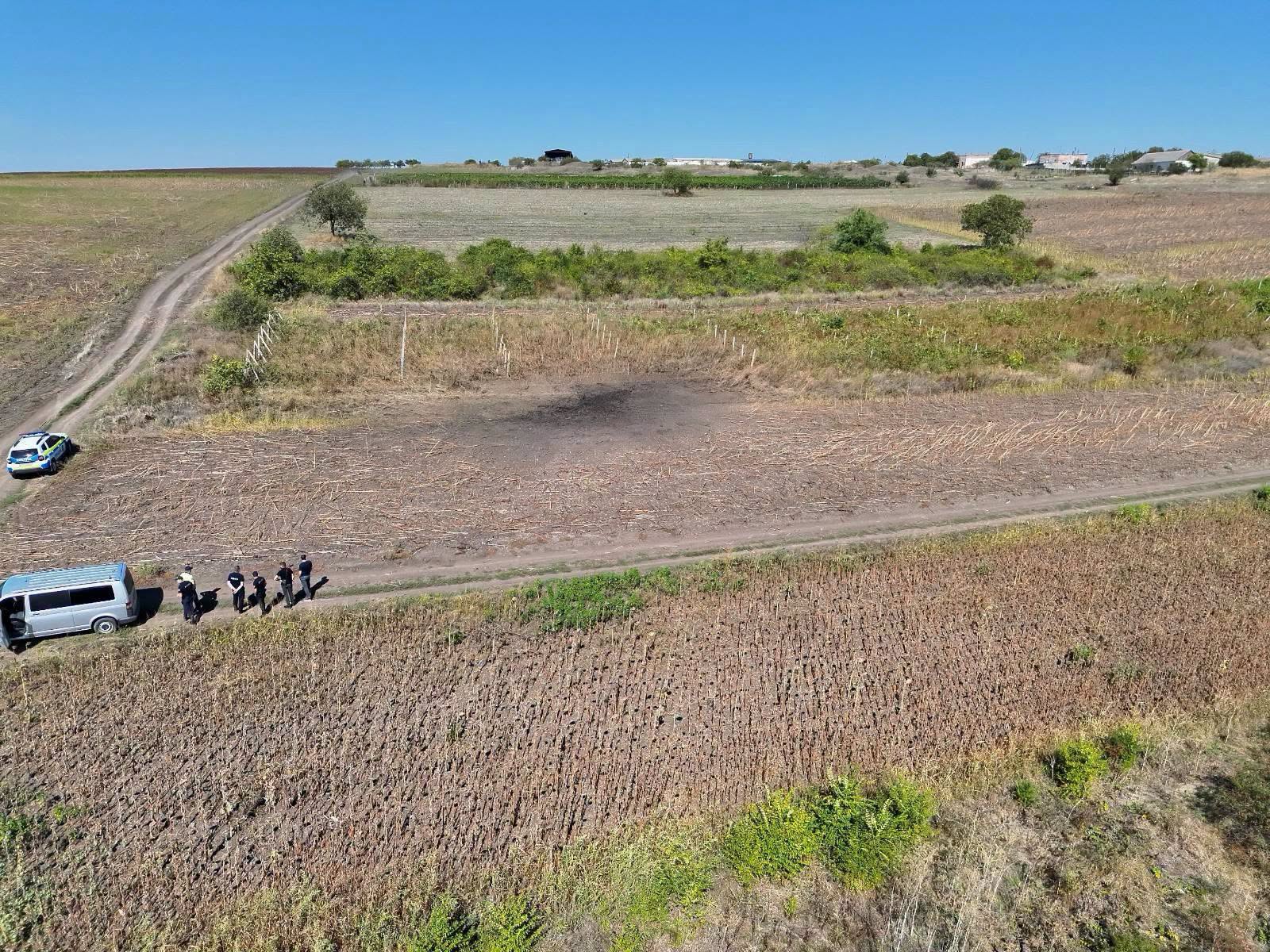 Aerial view of the scorched blast site in a field near Colonița, with a police vehicle and officers approaching on foot